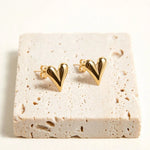 Gold puffed heart stud earrings on travertine with thin delicate posts