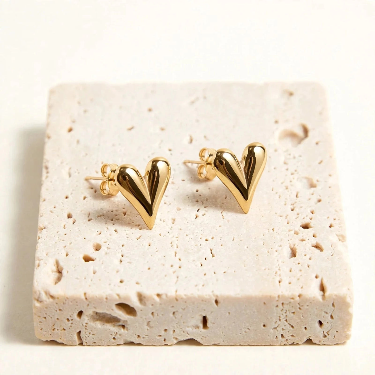 Gold puffed heart stud earrings on travertine with thin delicate posts