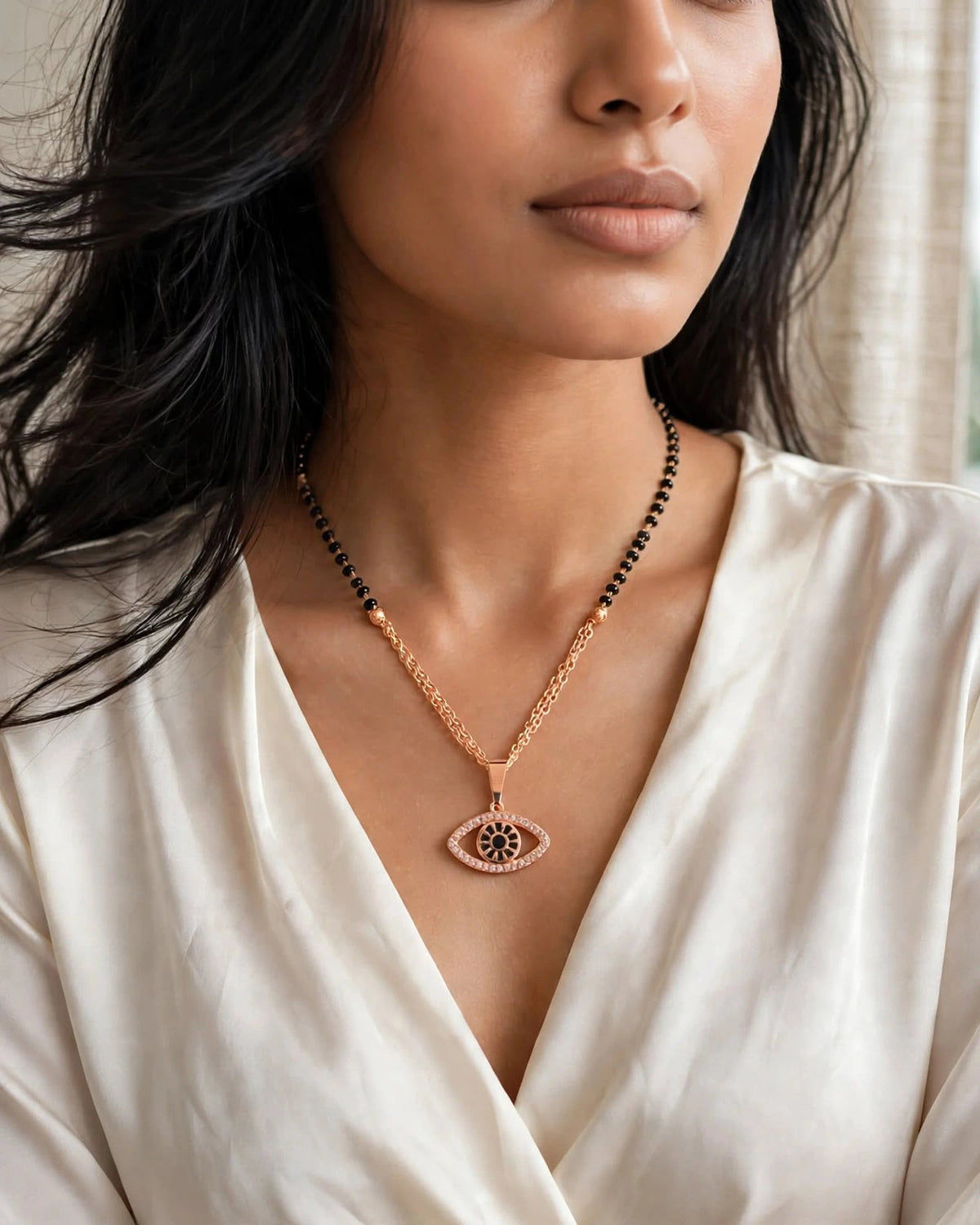 Indian woman in ivory satin V-neck blouse wearing rose gold evil eye mangalsutra necklace candid