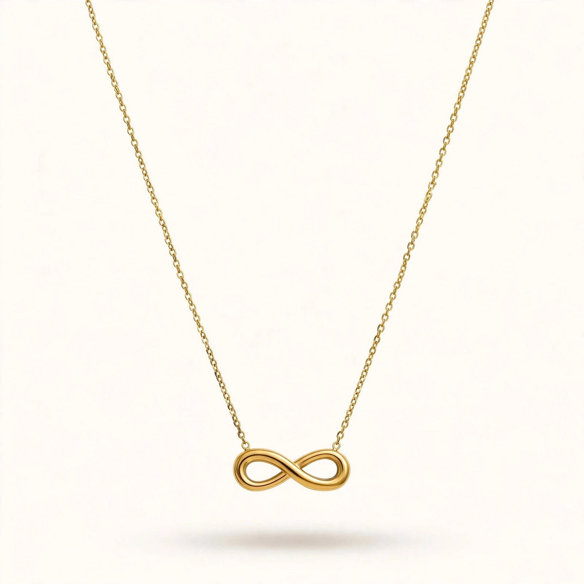 Gold infinity pendant necklace with cable chain in V drape on warm off-white