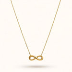 Gold infinity pendant necklace with cable chain in V drape on warm off-white