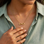 Indian woman in sage crisp shirt with smaller gold infinity necklace, hand below, face out of frame