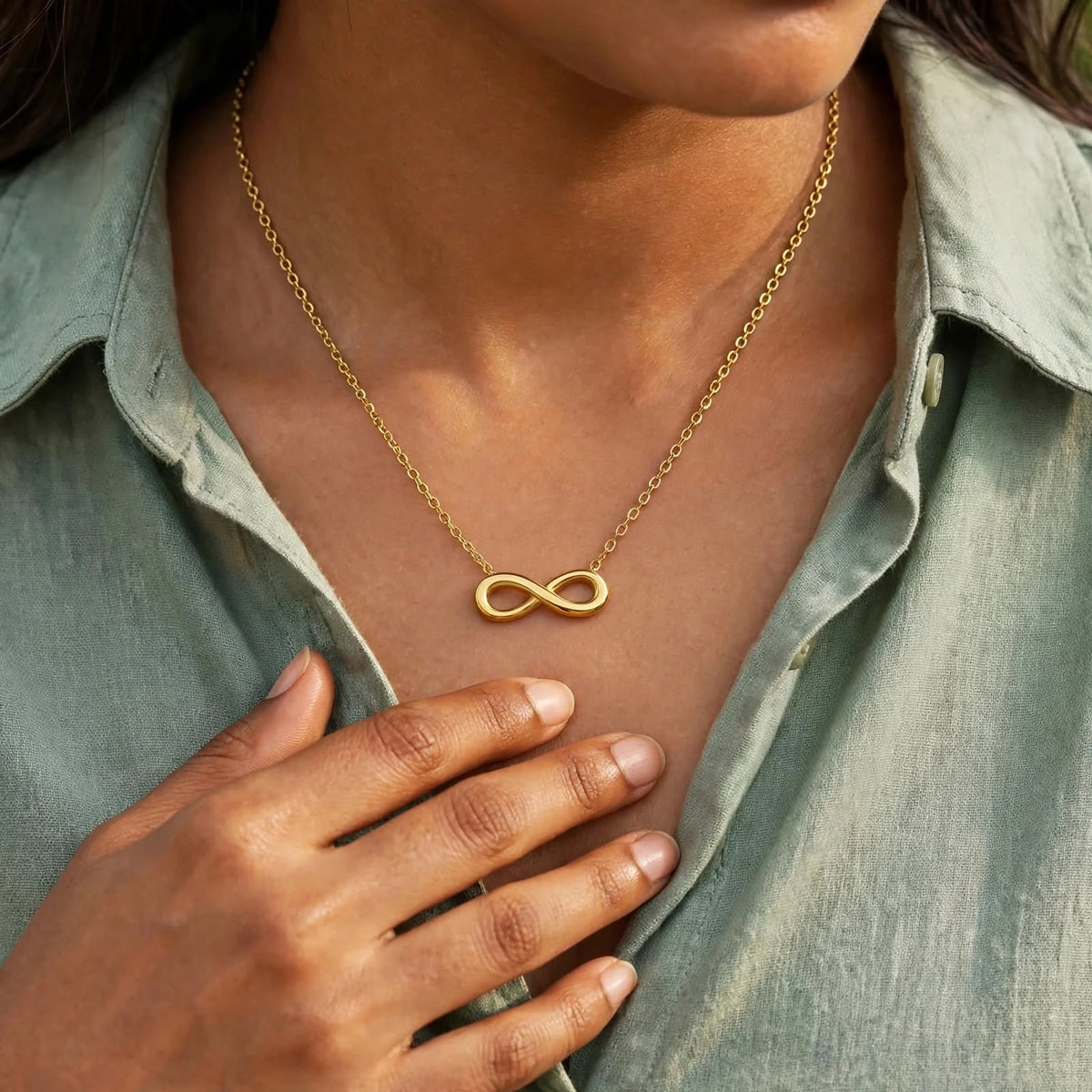 Indian woman in sage crisp shirt with smaller gold infinity necklace, hand below, face out of frame