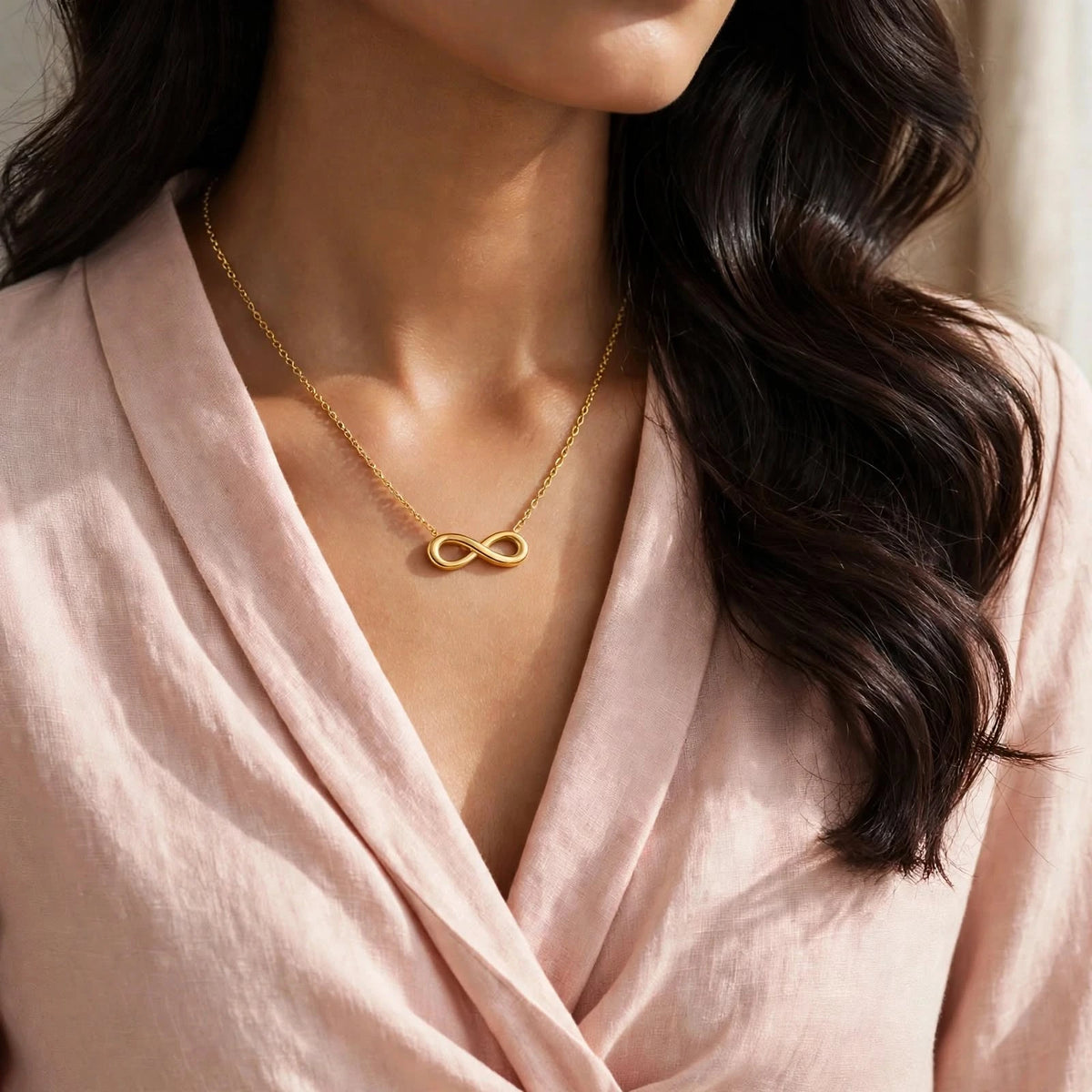 Indian woman in blush wrap blouse with smaller gold infinity necklace, face out of frame