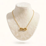 Gold infinity necklace on ivory velvet bust against warm-white background