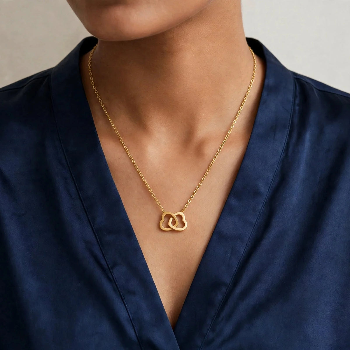 Indian woman in navy satin V-neck blouse wearing gold double heart pendant necklace.