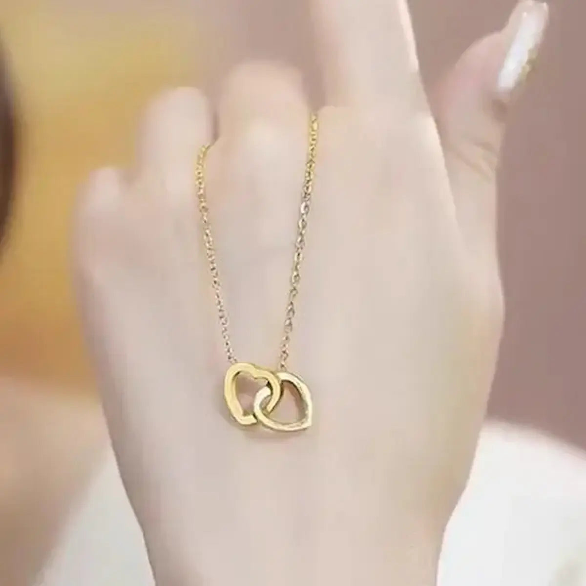 Hand holding gold double interlocked heart pendant necklace on delicate cable chain.