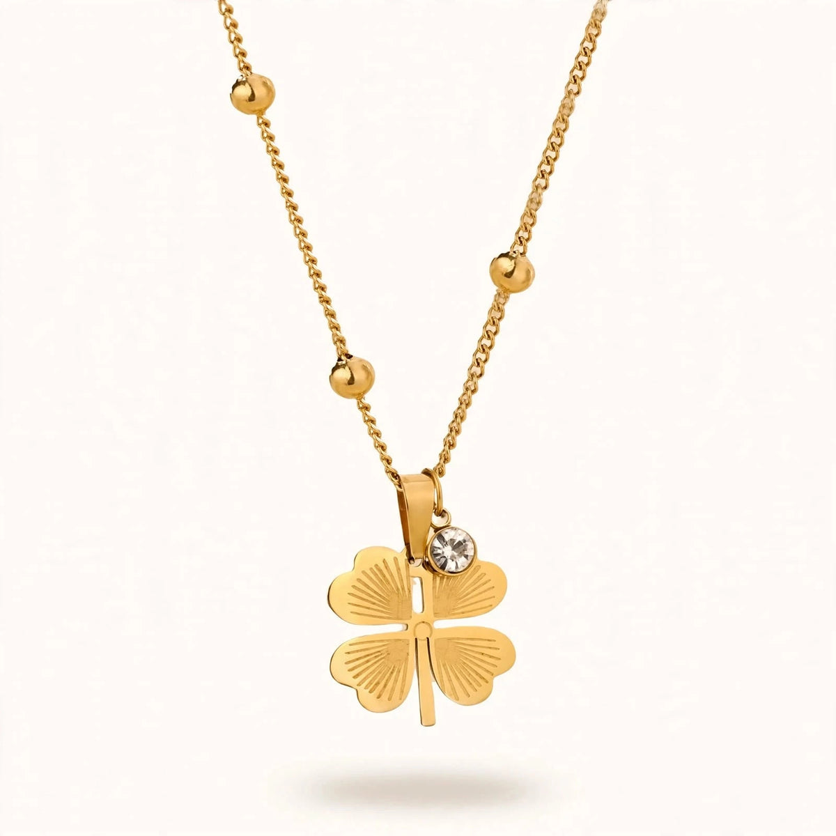 Gold four-leaf clover necklace with crystal charm floating on warm white background