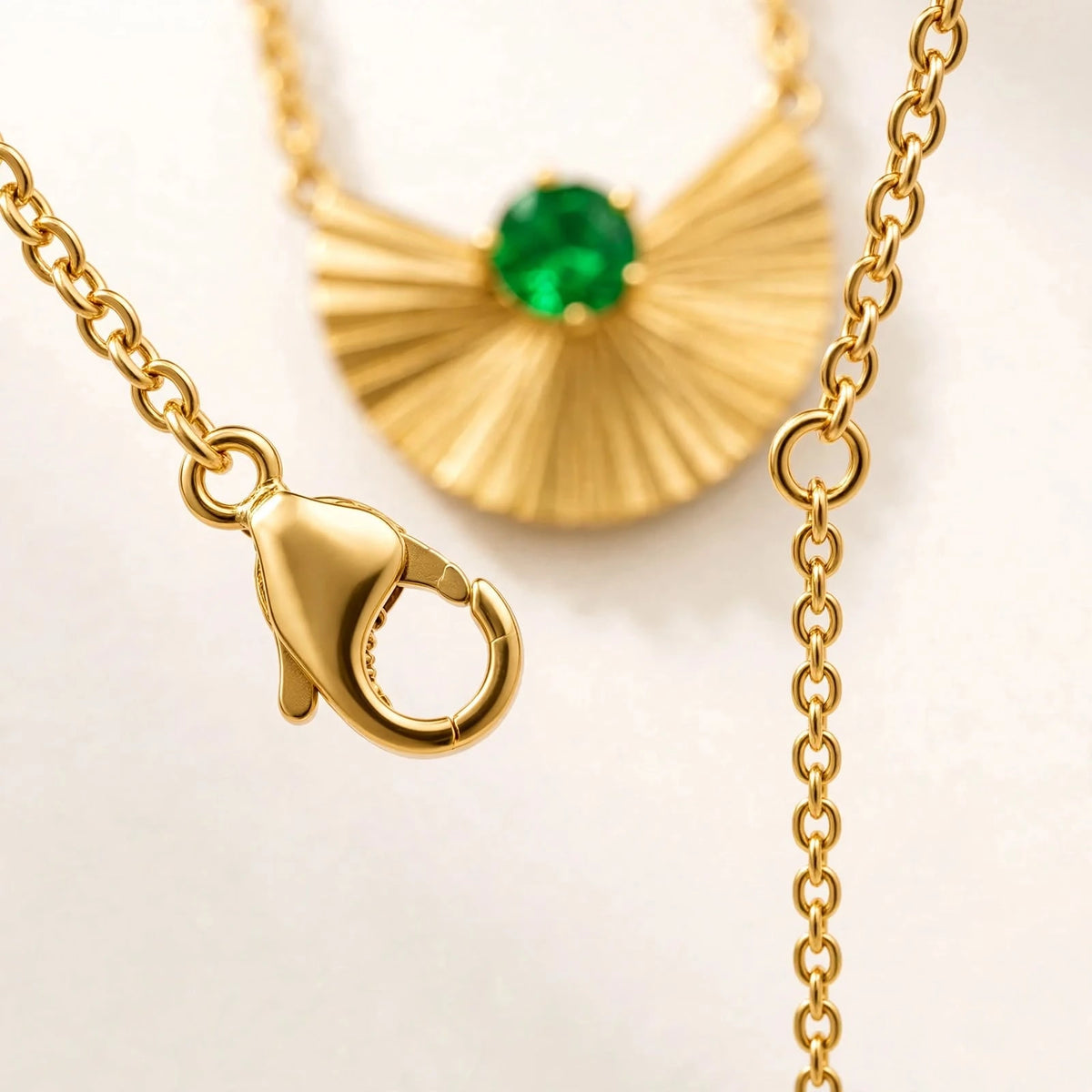 Close-up of gold lobster clasp and extension chain with emerald fan pendant