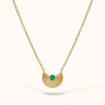 Gold fan pendant with emerald on cable chain on warm white background