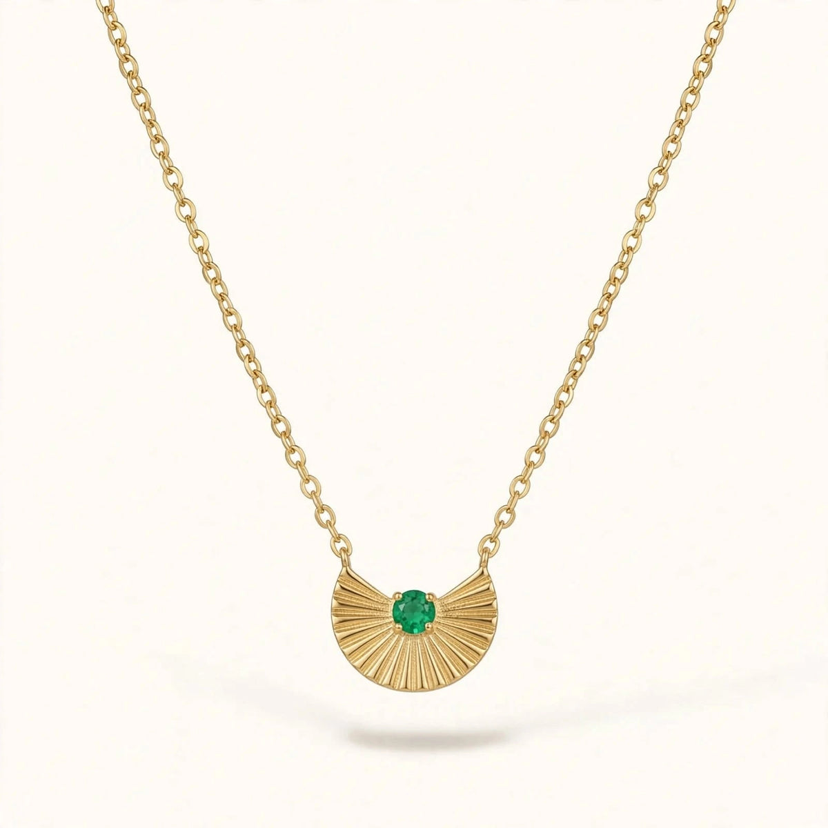 Gold fan pendant with emerald on cable chain on warm white background