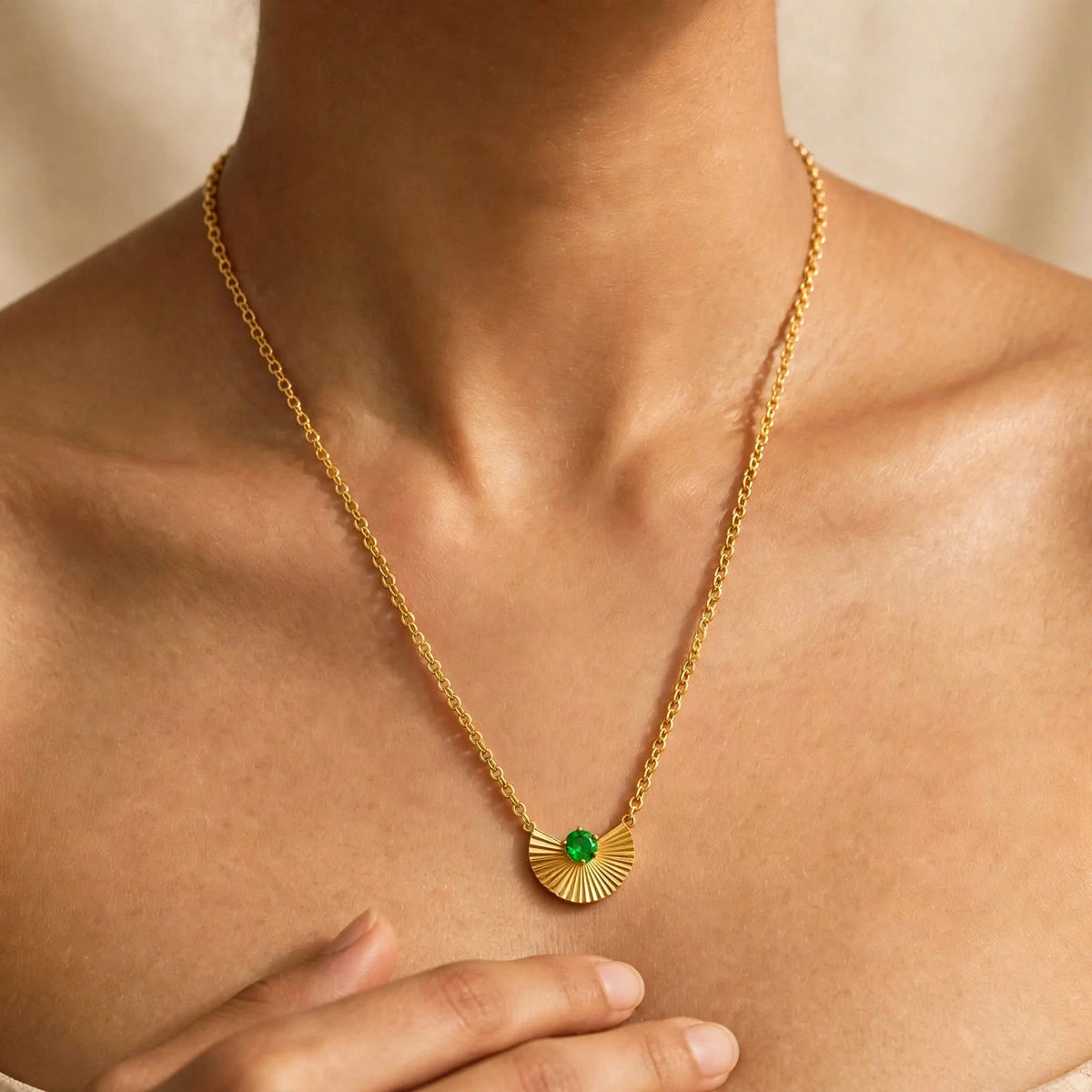 Gold fan pendant emerald necklace on model hand below pendant