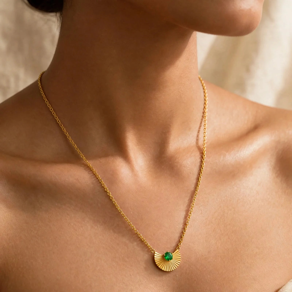 Gold fan pendant emerald necklace on model with flawless skin collarbones