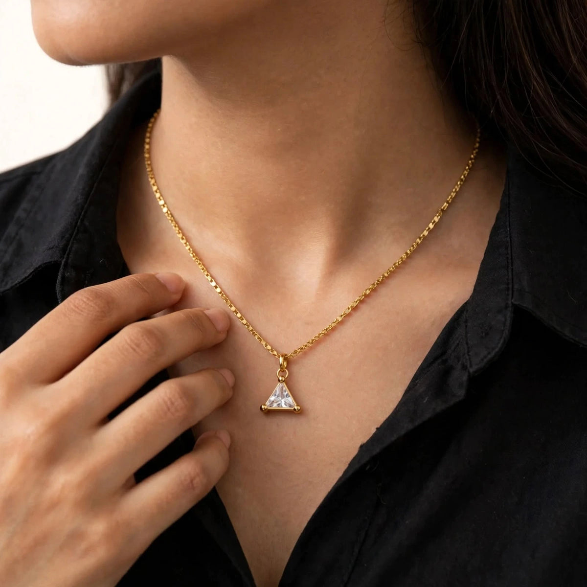Model in black cotton shirt touching collarbone wearing triangular crystal pendant