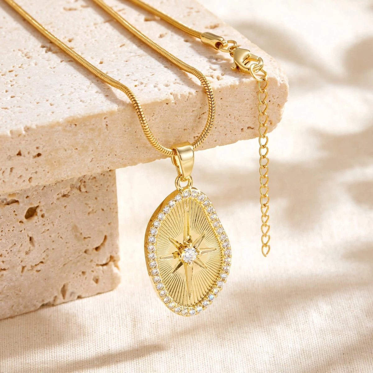 Gold sunburst pendant necklace elevated on beige stone blocks on cream linen