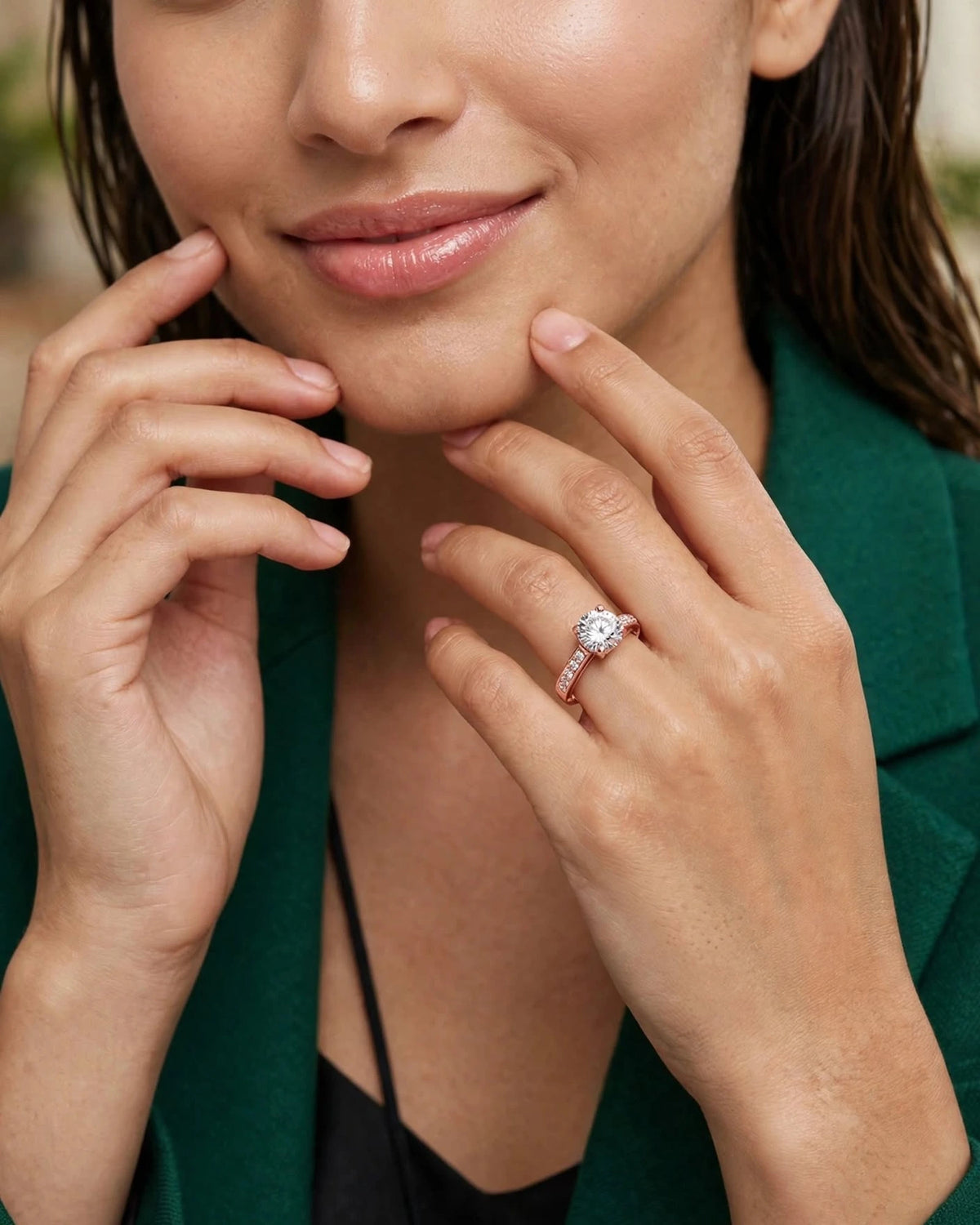 Close-up of rose gold solitaire ring on hand near lips, emerald blazer