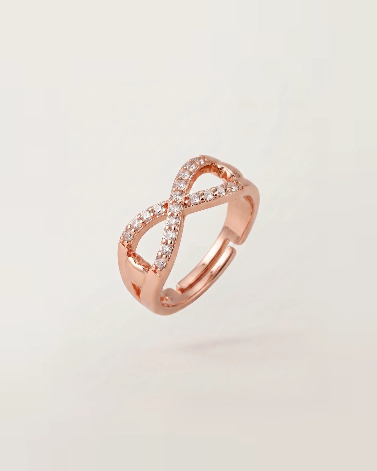 Rose gold infinity ring with solid right side and adjustable open back band on warm off-white background.