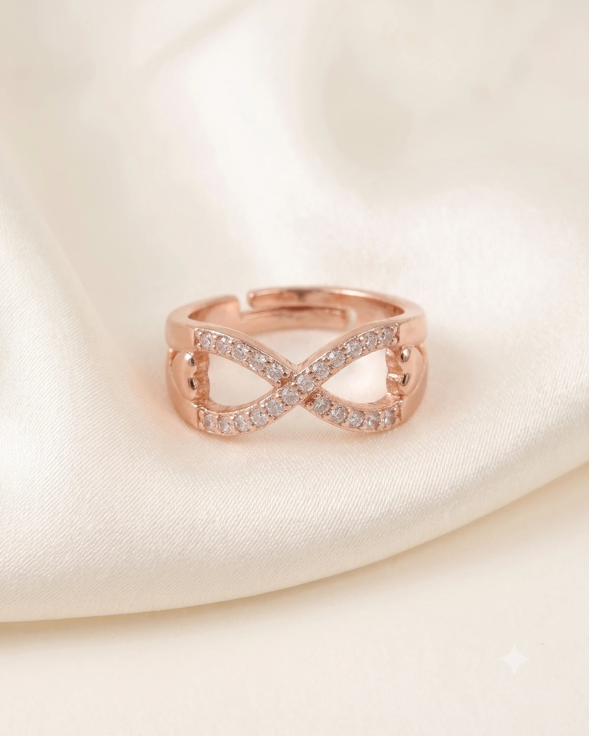 Rose gold infinity ring laying flat on a soft fold of ivory silk against a warm white background.