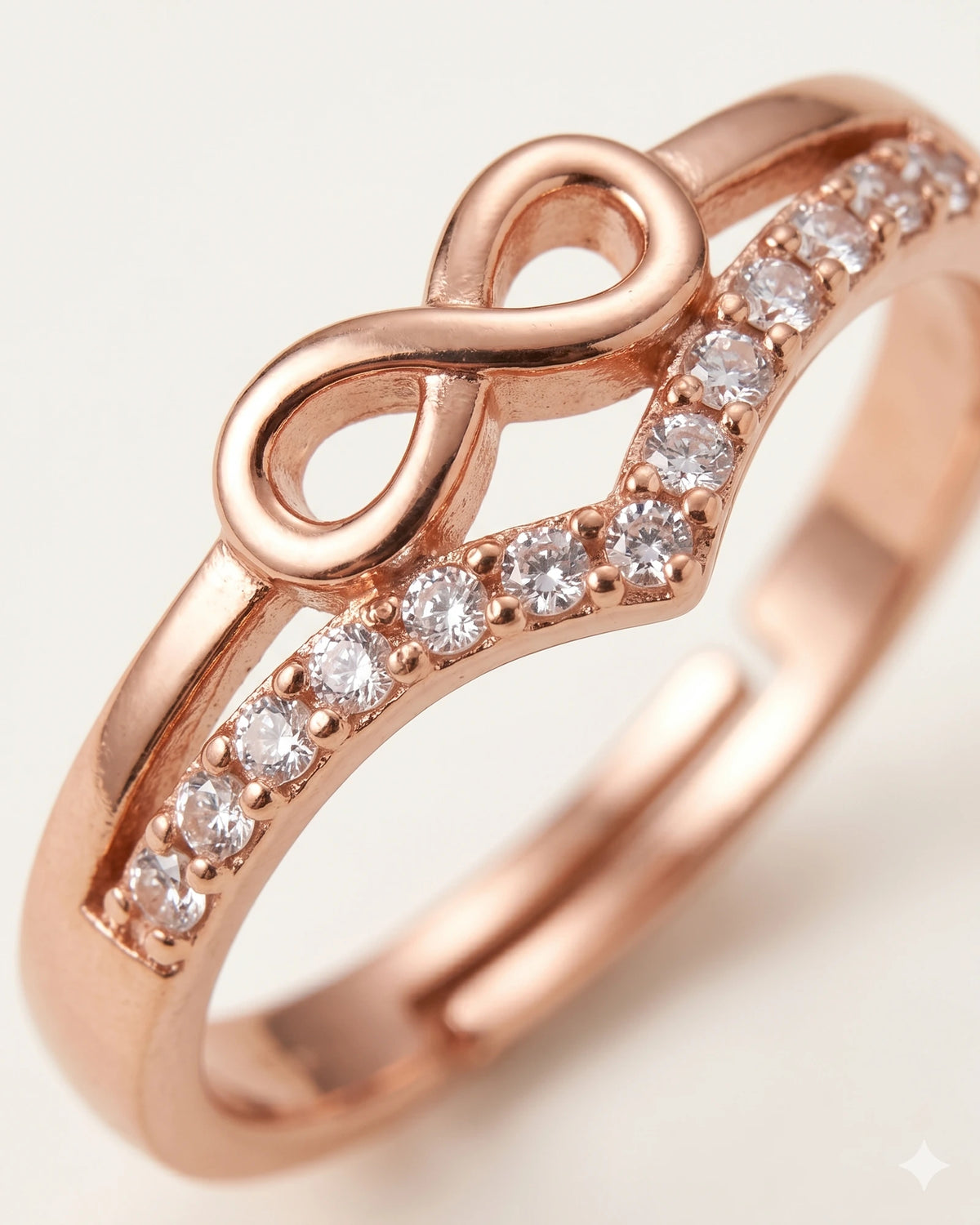 Extreme macro close-up of rose gold infinity ring with CZ stones, showing center design details on off-white background.