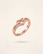 Rose gold infinity ring with CZ stones floating on an off-white background.