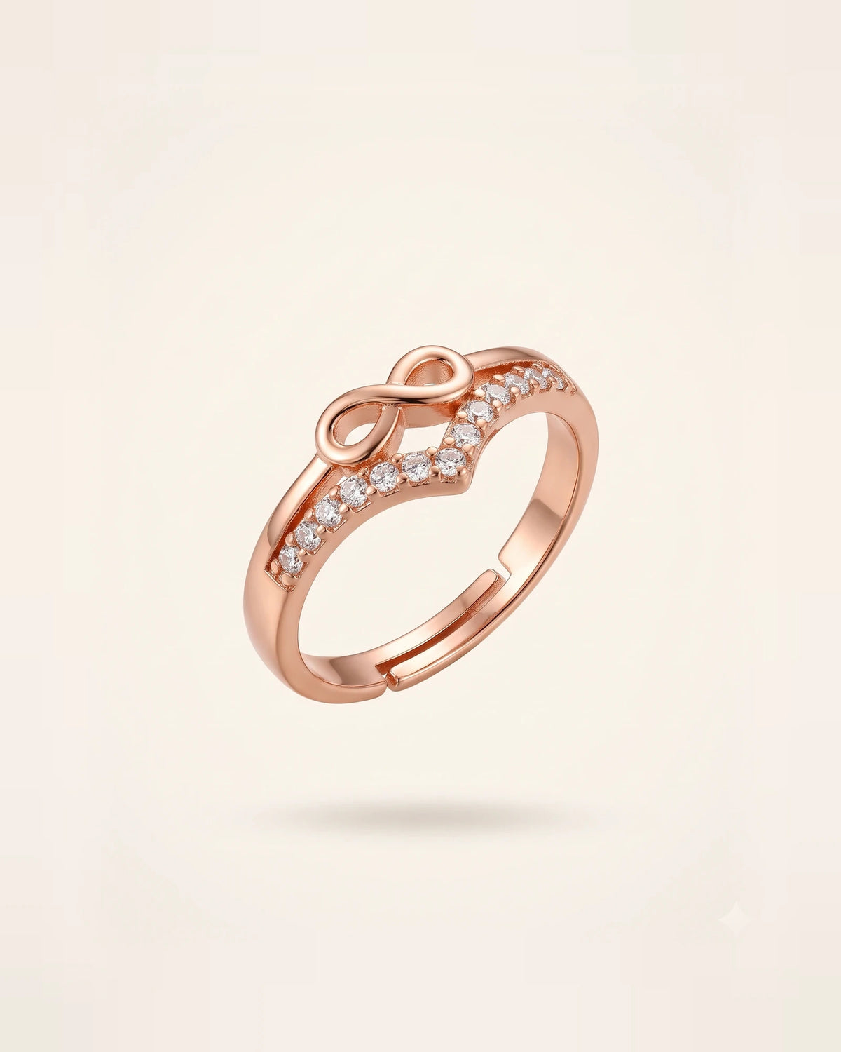 Rose gold infinity ring with CZ stones floating on an off-white background.