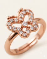 Extreme macro close-up of a rose gold butterfly ring with CZ stones, showing center design details on off-white background.
