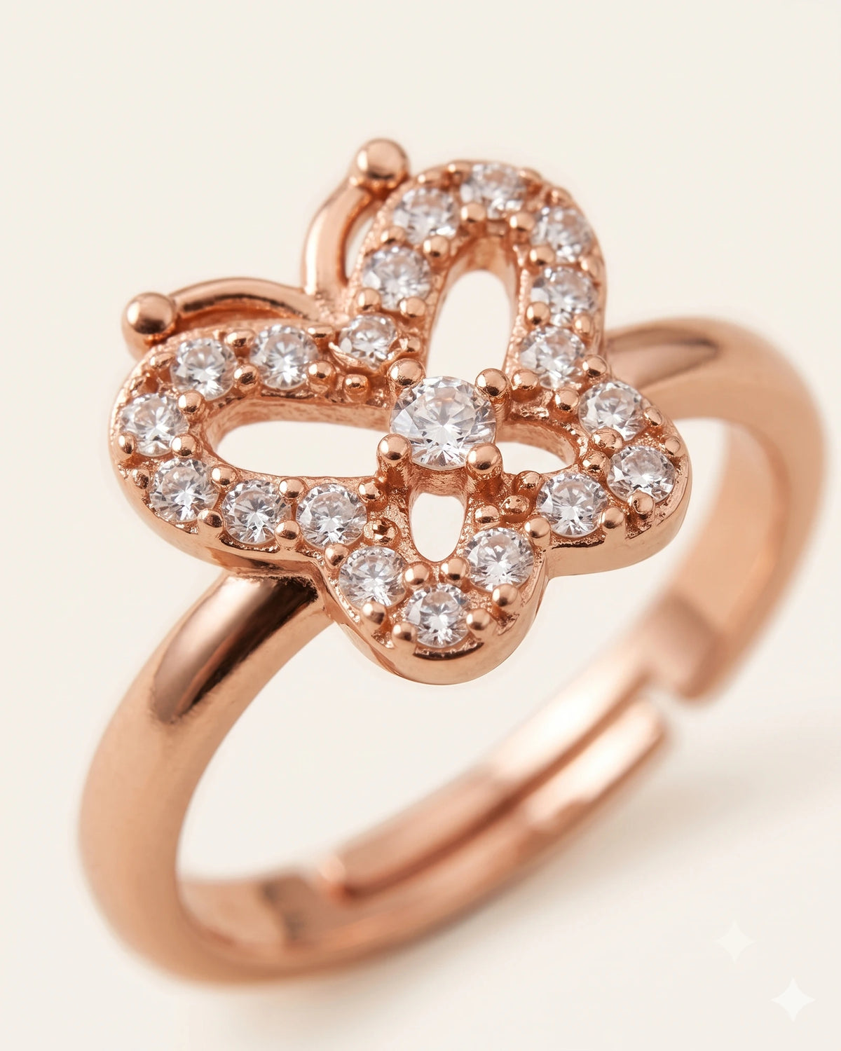 Extreme macro close-up of a rose gold butterfly ring with CZ stones, showing center design details on off-white background.