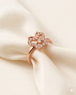Rose gold butterfly ring resting on ivory silk against a warm-white background.