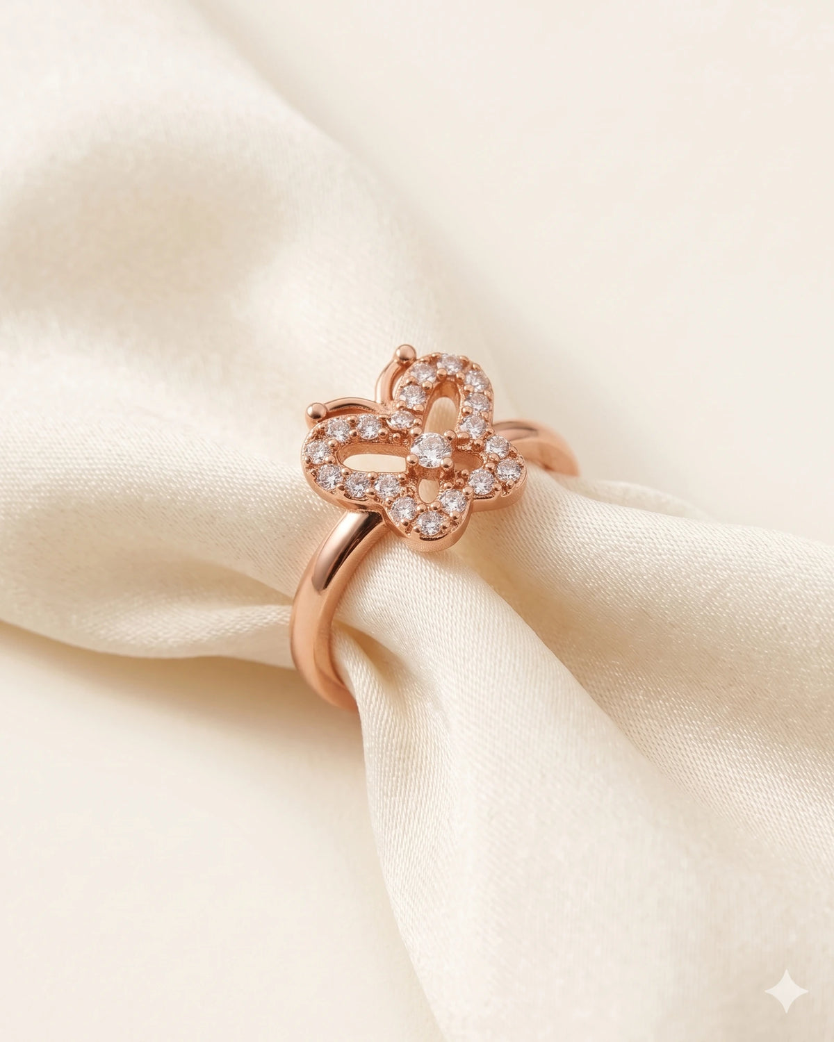 Rose gold butterfly ring resting on ivory silk against a warm-white background.