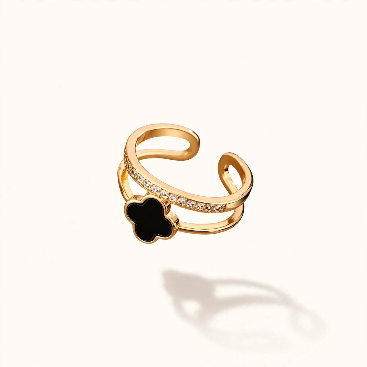 Gold open ring with black clover and crystal band floating on off-white background