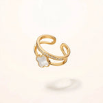 Gold open ring with white clover and crystal band floating on off-white background
