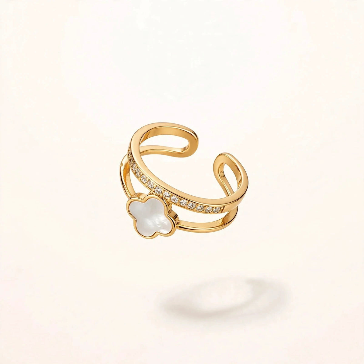 Gold open ring with white clover and crystal band floating on off-white background