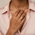 Indian woman in blush silk shirt touching collarbone wearing white clover gold ring