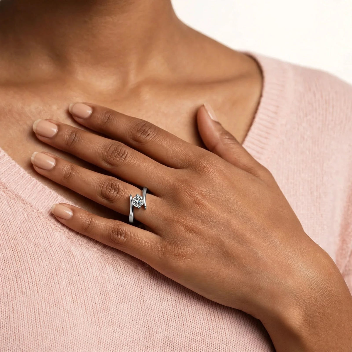 Indian woman hand on chest below collarbone wearing silver open bypass ring blush sweater.