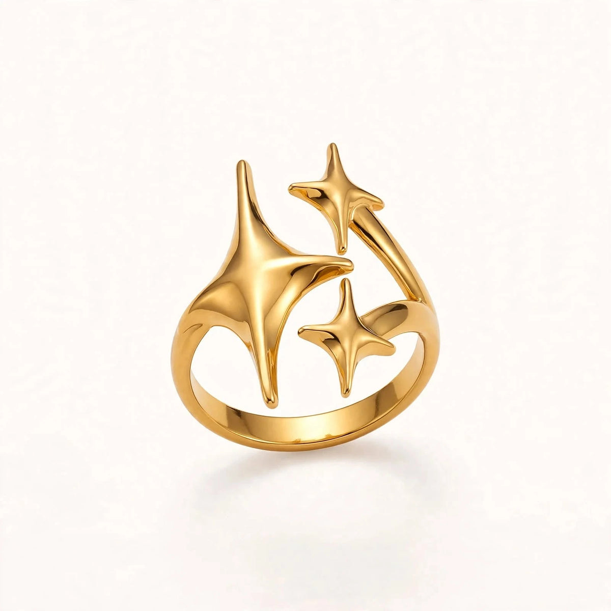 Gold open ring with three starbursts, opening at top, floating on warm off-white background