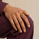 Indian woman in wine cotton shirt with gold triple star ring resting on raised knee