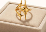 Gold triple star ring on beige velvet tray against warm white background