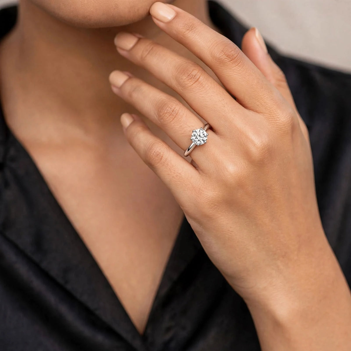 Close-up of hand with pea-sized solitaire adjustable ring near jaw, black satin blouse, neutral backdrop