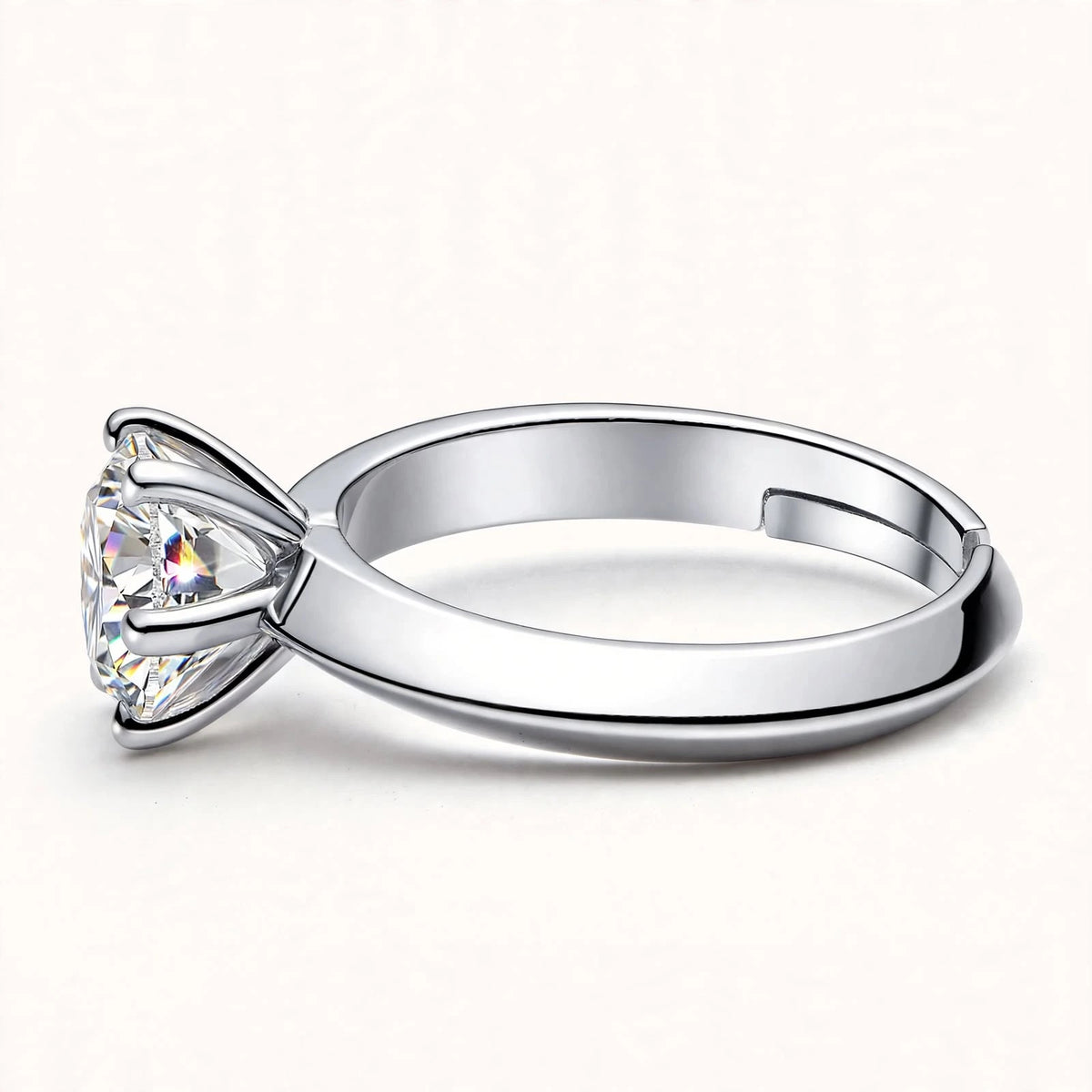 Silver adjustable solitaire ring lying horizontal on off-white surface showing side profile and inner band