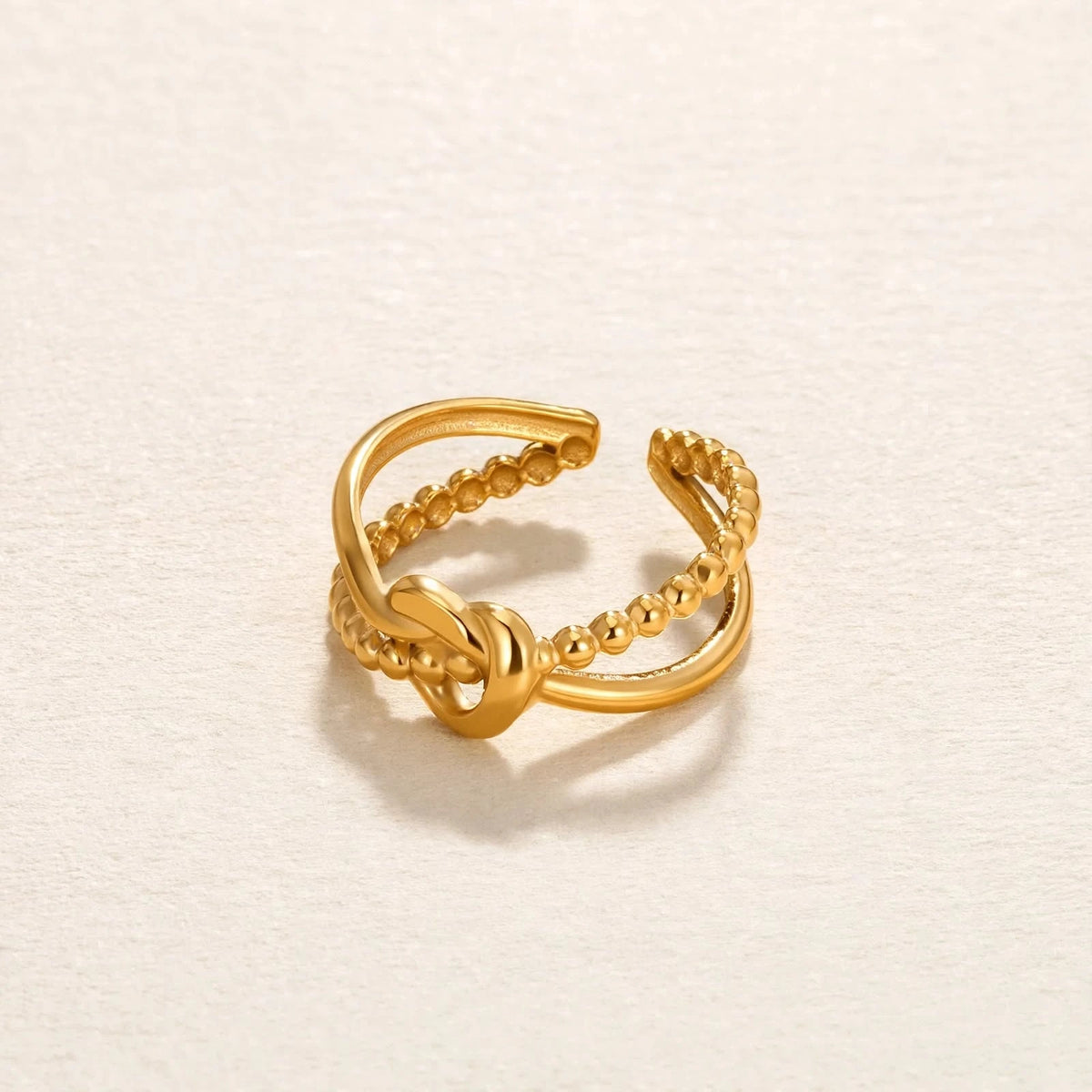 Gold knot adjustable open ring on textured cream paper with warm white background