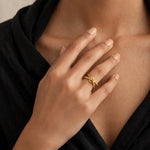 Fingertips at collarbone in black wrap blouse wearing gold knot adjustable open ring