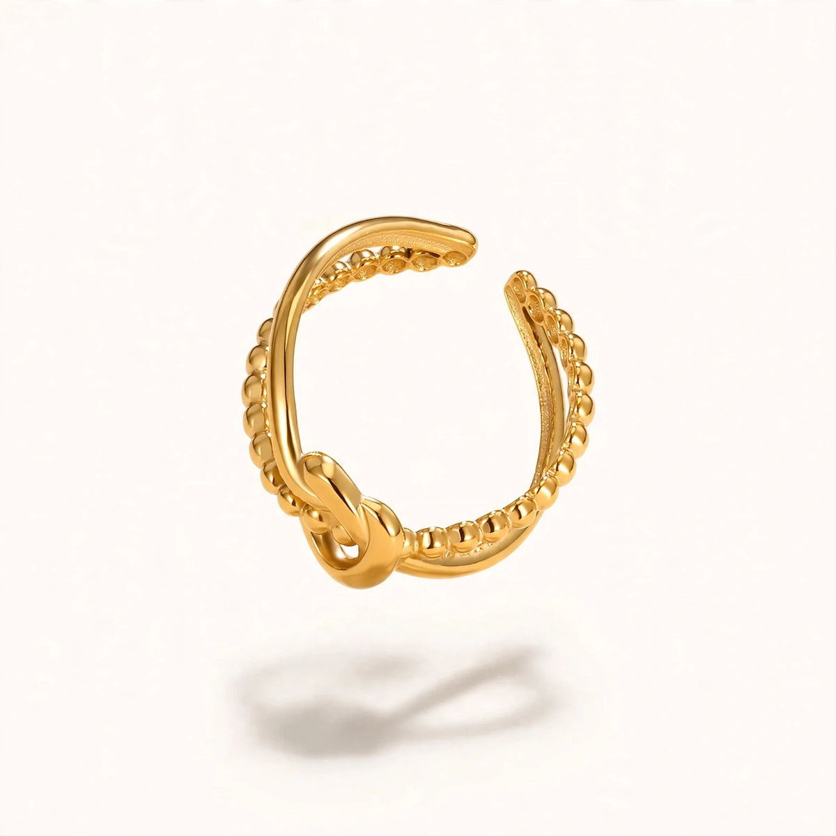 Gold knot adjustable open ring with beaded band floating on warm off-white background
