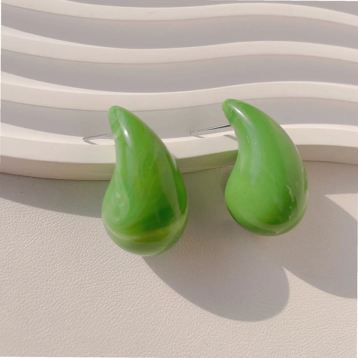 Two glossy green drop-shaped earrings displayed against a textured white background, highlighting their vibrant color and smooth finish.