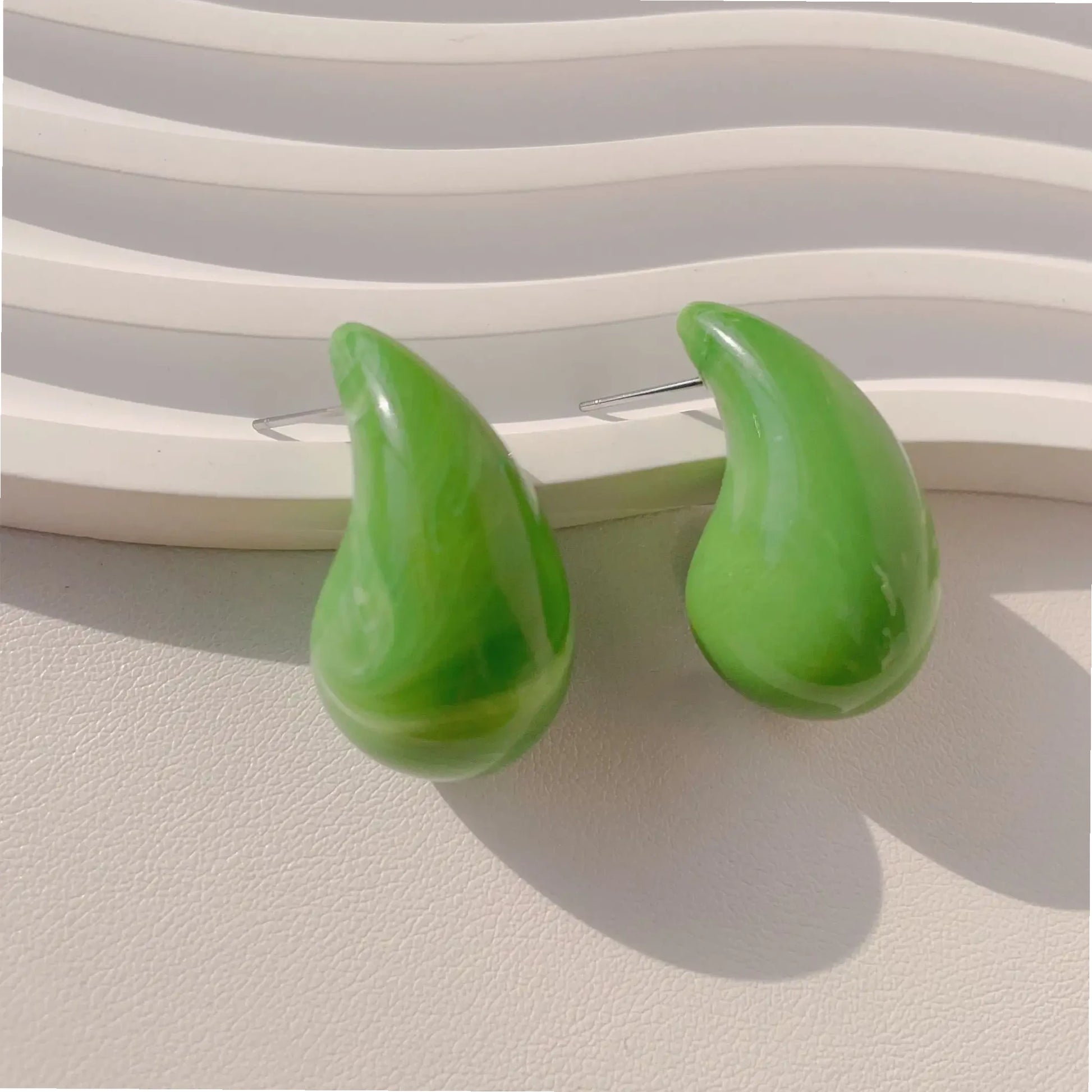 Two glossy green drop-shaped earrings displayed against a textured white background, highlighting their vibrant color and smooth finish.