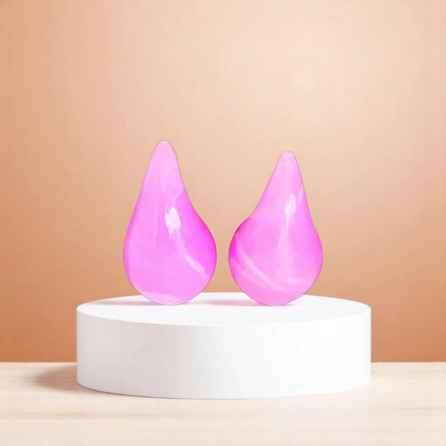 Two glossy, teardrop-shaped pink beauty sponges displayed on a white circular pedestal against a soft beige background.