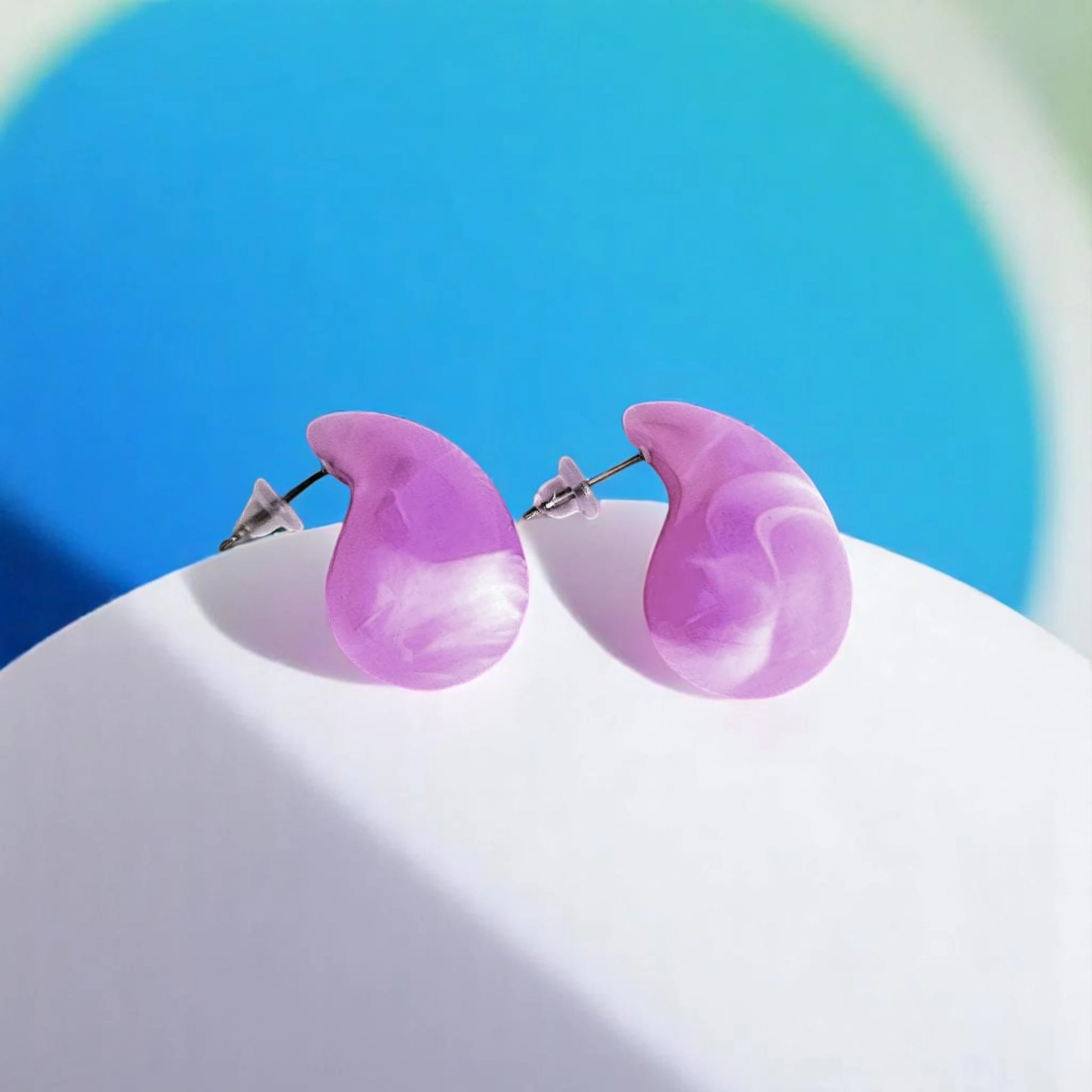 Two stylish, marbled purple resin earrings on a white surface, set against a soothing blue background.
