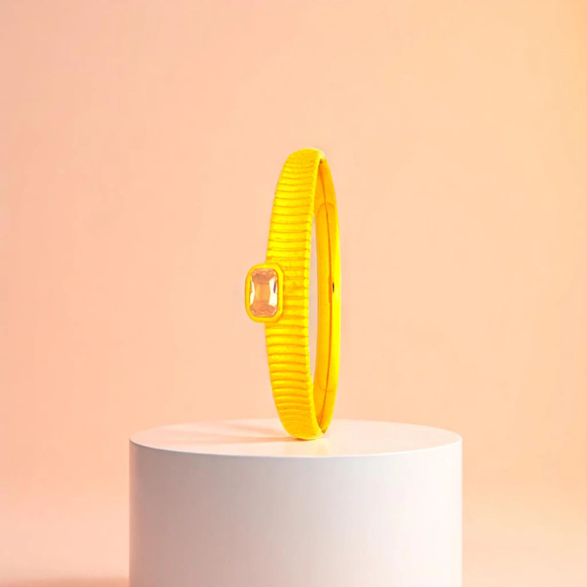 Bracelet displayed on a white pedestal against a soft peach background.