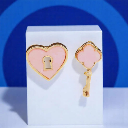 Gold heart and key pins with pink enamel accents, displayed on a white pedestal against a blue background.