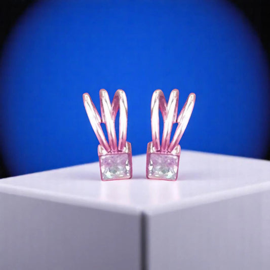 A pair of unique pink earrings featuring flexible leaf-like designs and square, translucent gemstones, set against a blue background.