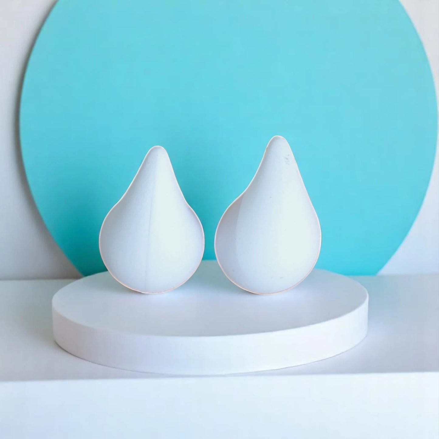 Two white teardrop-shaped sculptures on a circular pedestal, set against a bright turquoise background.